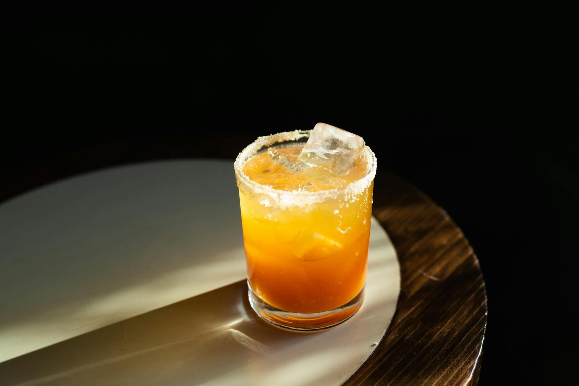 Szklanka pomarańczowego drinka z kostkami lodu i solą na brzegu na stole