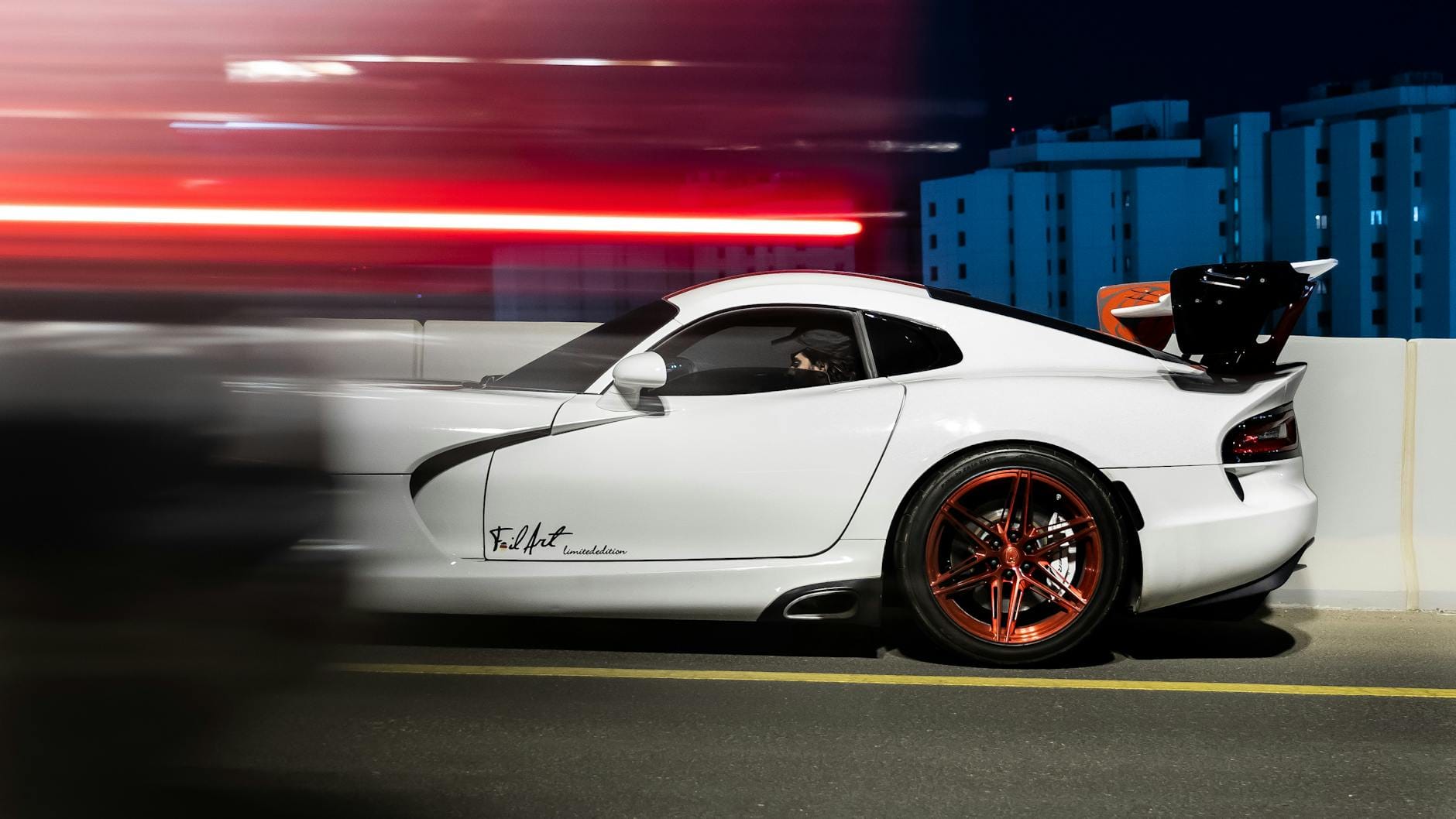 Białe sportowe auto pędzące nocą po oświetlonym mieście