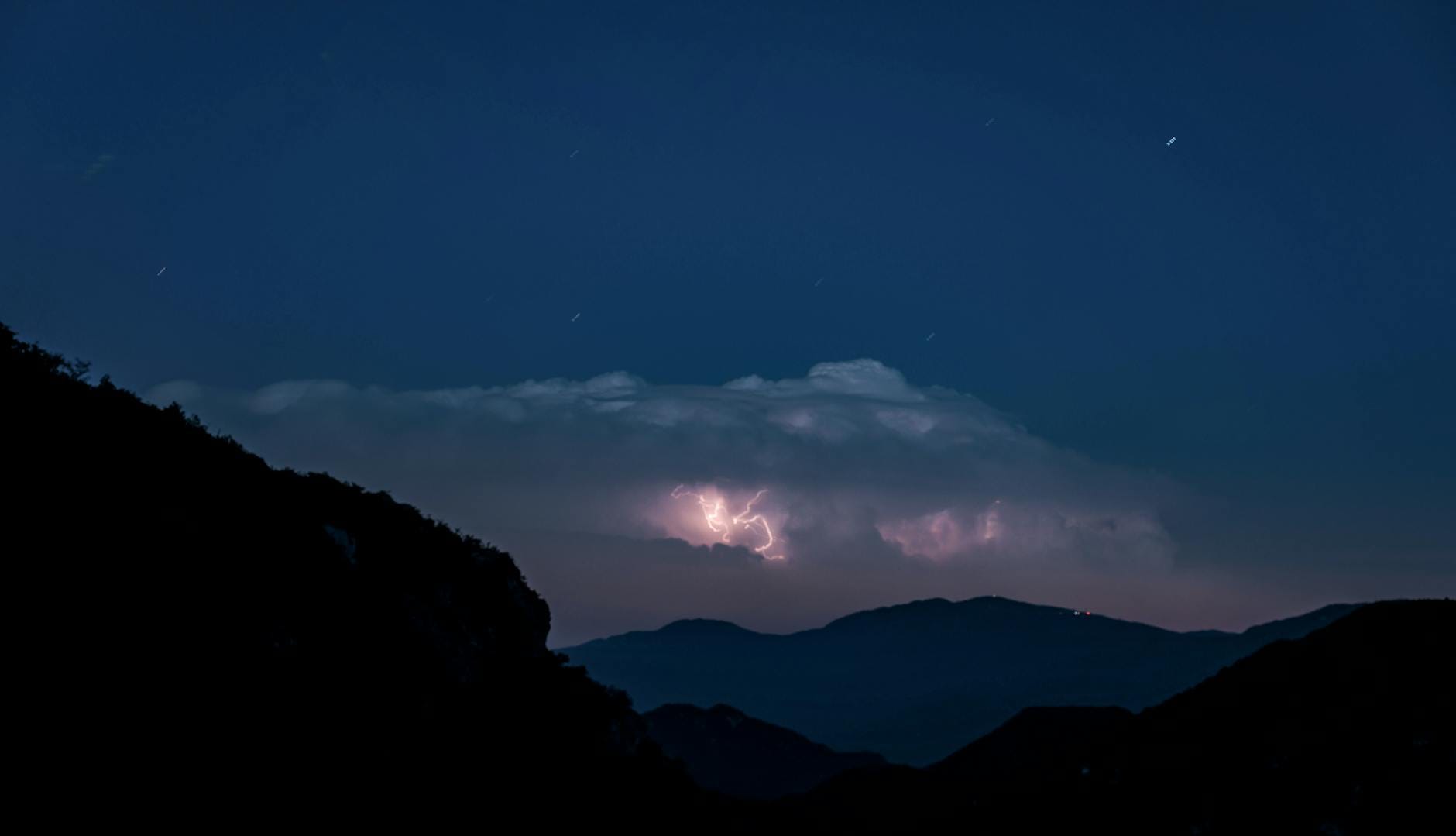 Dlaczego czasem słychać grzmot, choć burzy „nie widać” na niebie? Góry nocą oświetlone błyskawicą na ciemnym, burzowym niebie