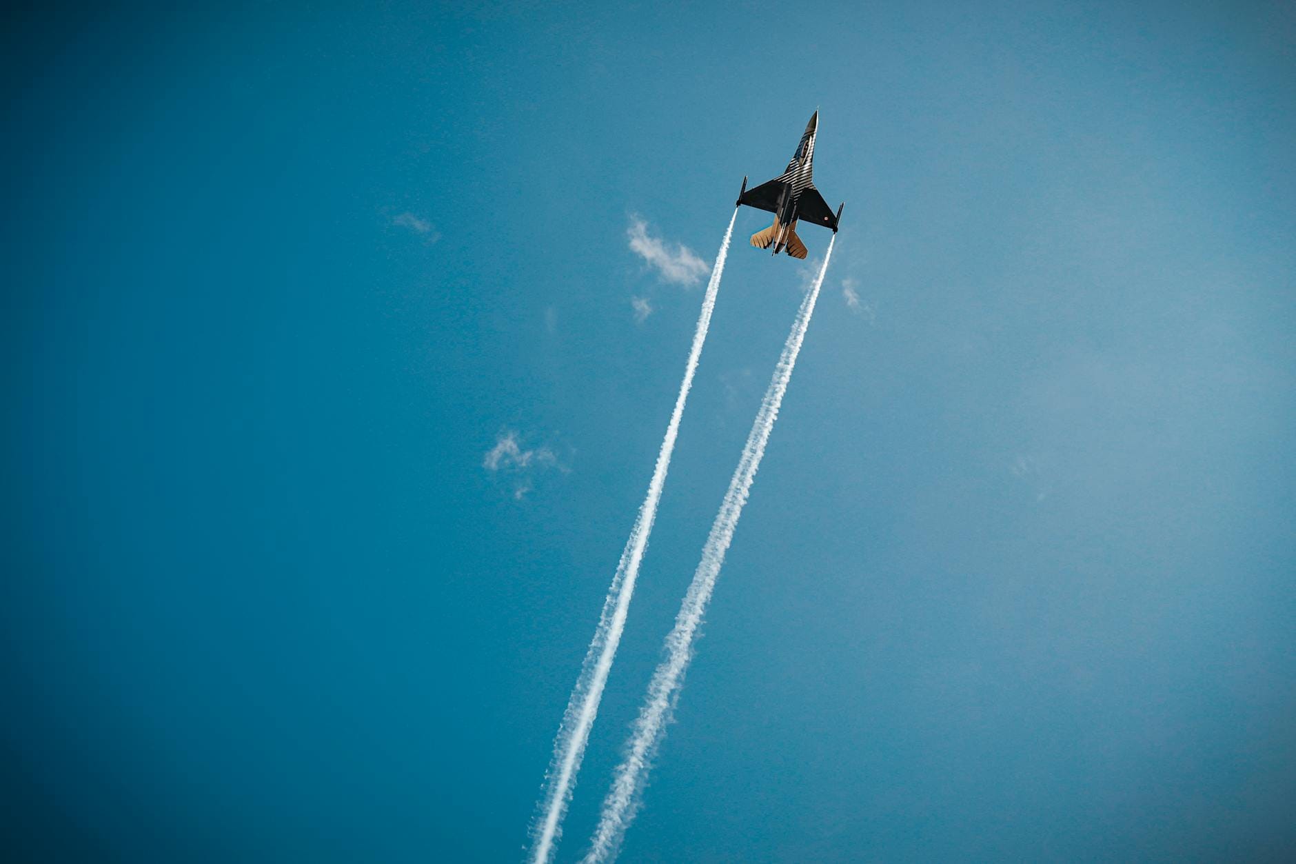 Myśliwiec z białymi smugami kondensacyjnymi na błękitnym niebie