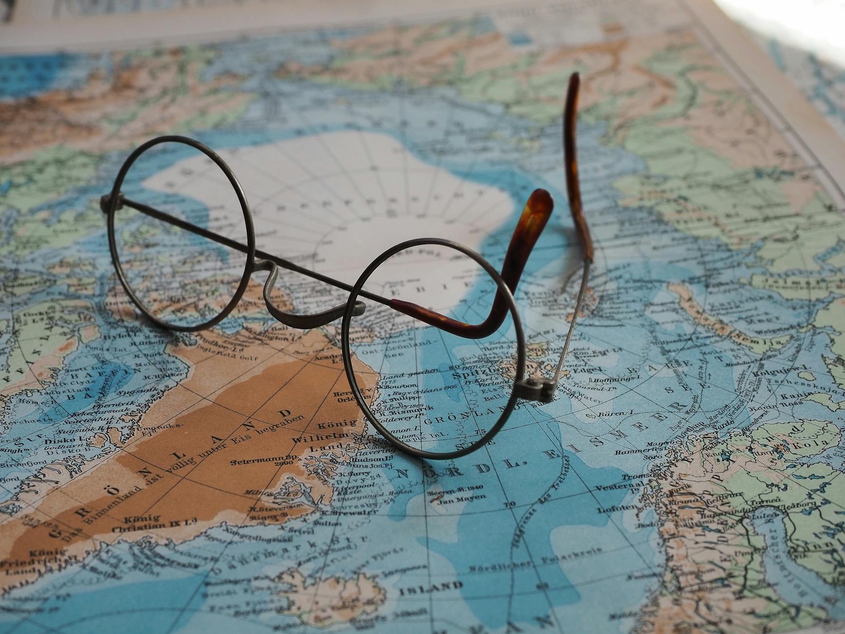 Okrągłe okulary leżące na mapie świata z Europą i Grenlandią