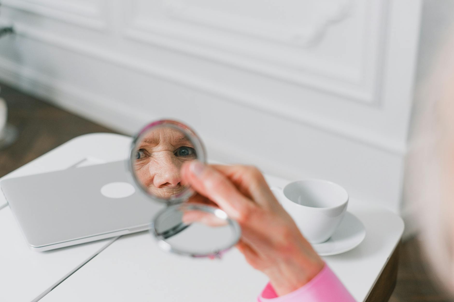Starsza kobieta w domu spogląda w twarz odbitą w lusterku kieszonkowym
